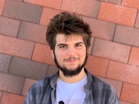 a man with a beard standing in front of a brick wall