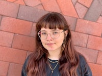 a woman wearing glasses and a black shirt in front of a brick wall