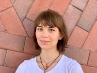 a woman wearing a white t - shirt standing in front of a brick wall