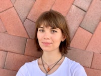 a woman wearing a white t - shirt standing in front of a brick wall